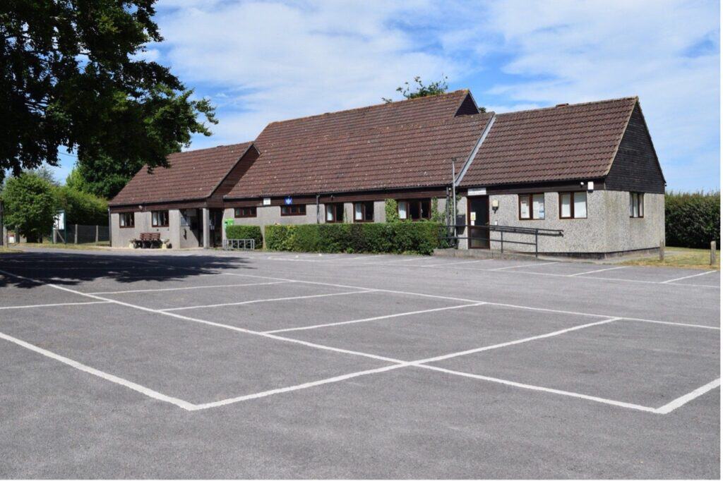 Wellow Village Hall building with parking lot and clear sky.