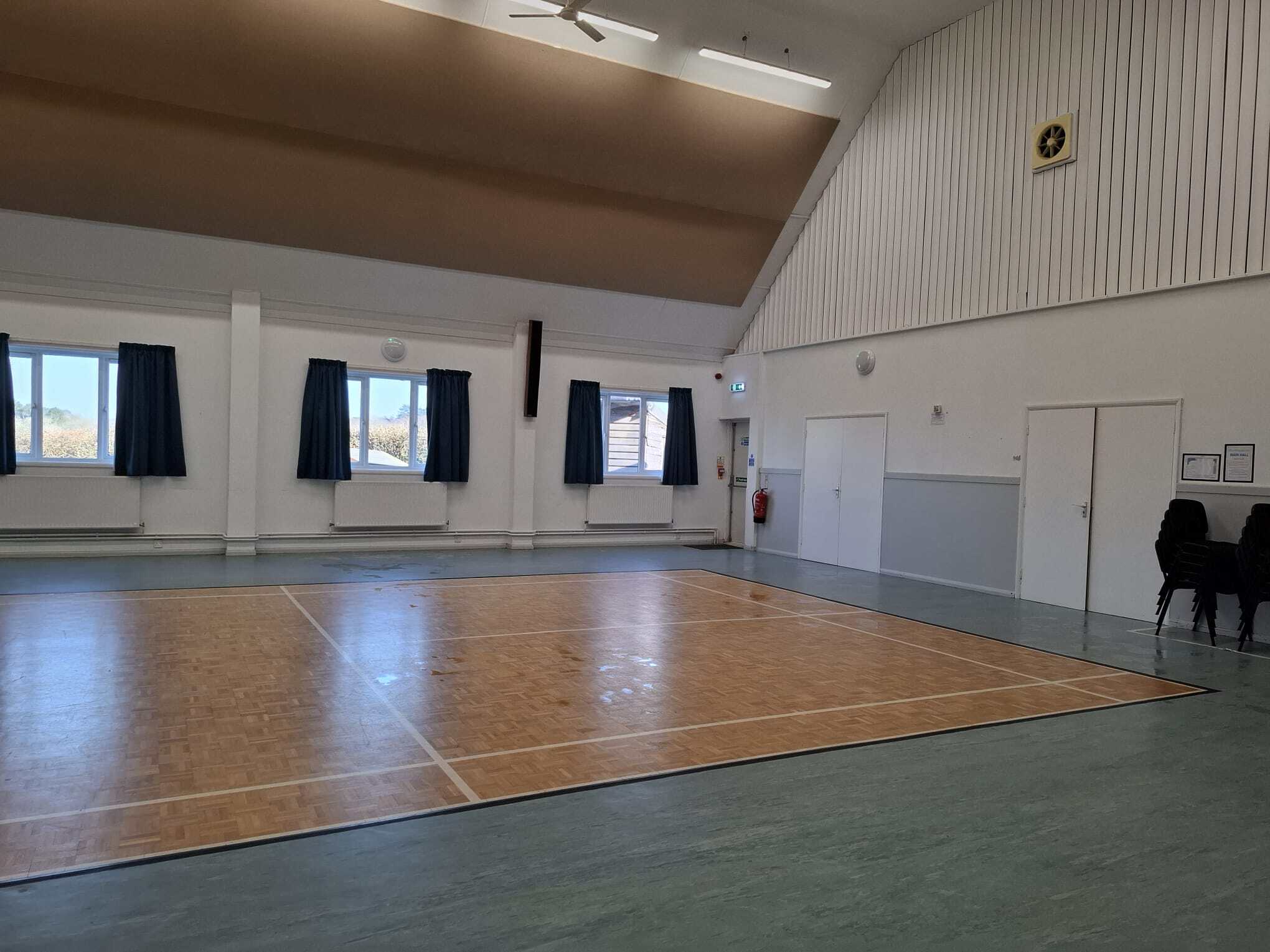 Indoor sports hall at Wellow Village Hall with wooden flooring and large windows.