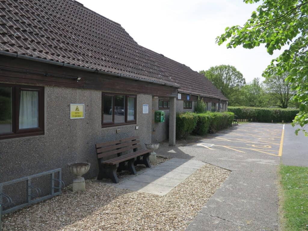 Wellow Village Hall building with parking area and greenery.