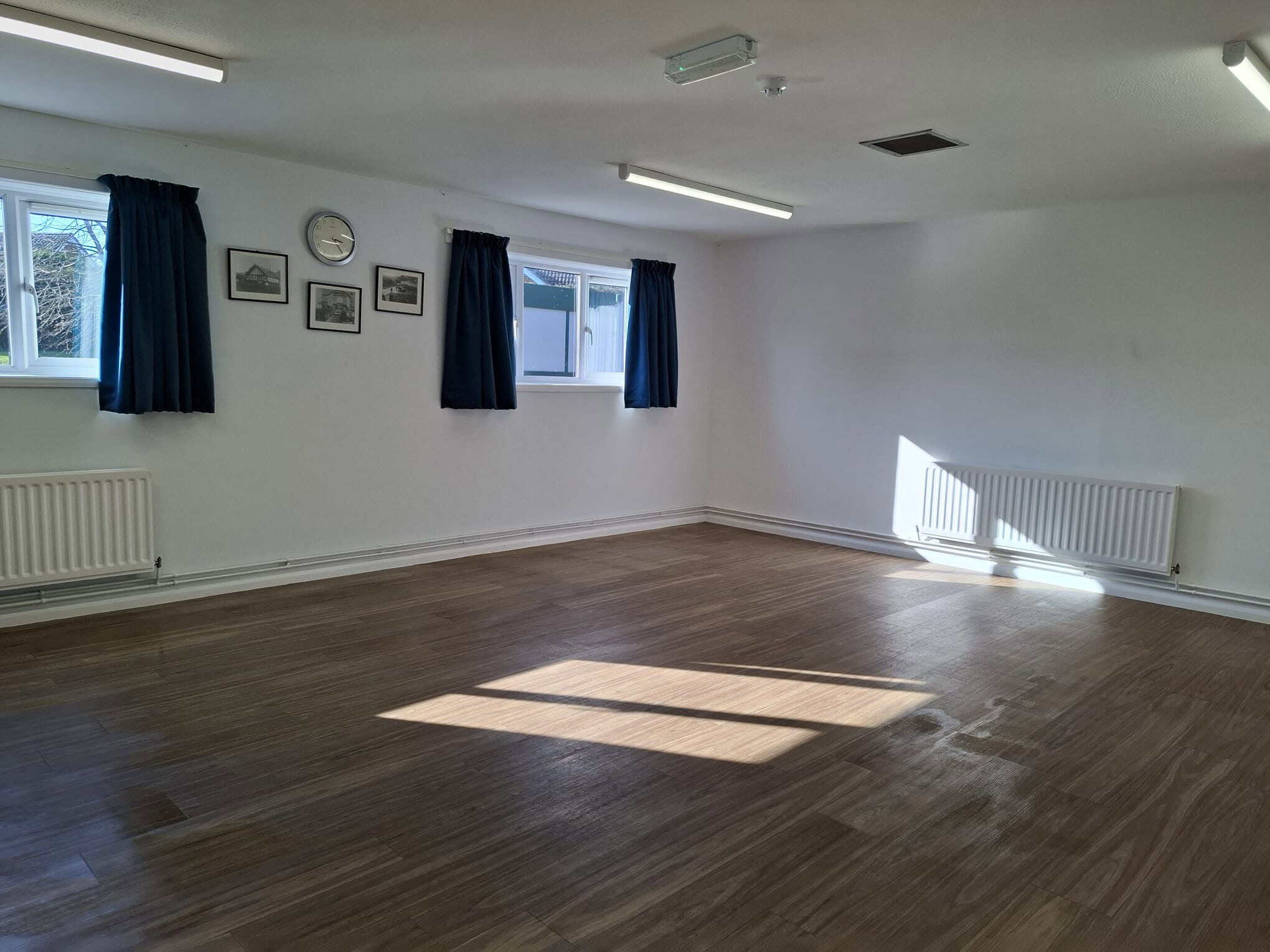 Community hall interior with wooden flooring, white walls, and blue curtains, ideal for events and g.